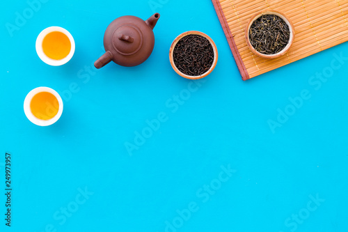 Chinese tea ceremony concept. Tea pot, tea cup, dry tea leaves, bamboo mat on blue background top view copy space pattern