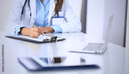Unknown doctor woman filling up medical form while sitting at the desk in hospital office. Physician at work. Medicine and health care concept © rogerphoto