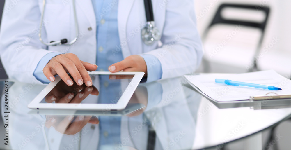 Female doctor hands using digital tablet while sitting at glass desk at hospital office. Medicine and healthcare concept Female doctor hands using digital tablet while sitting at glass desk at hospital office. Medicine and healthcare concept