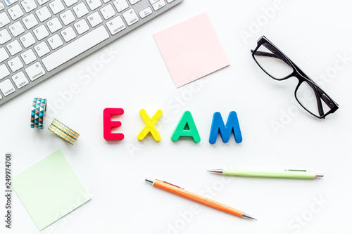 Preparing to exam. Word exam lined with colorful letters near computer keyboard and supplies on white background top view