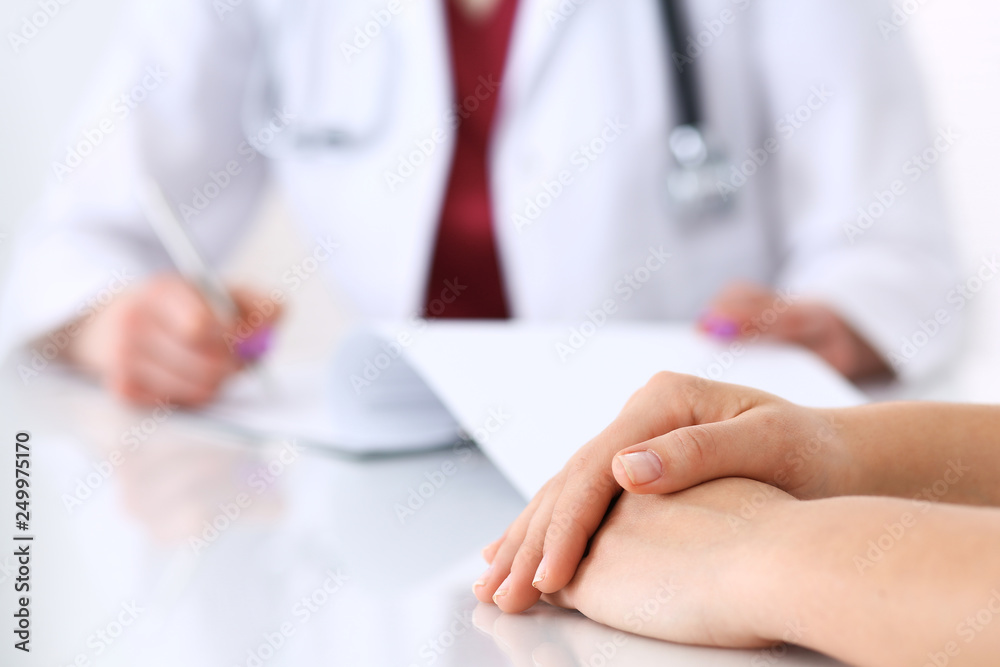 Unknown doctor woman consulting patient while filling up an application form at the desk in hospital. Just hands close-up. Medicine and health care concept Unknown doctor woman consulting patient while filling up an application form at the desk in hospital. Just hands close-up. Medicine and health care concept