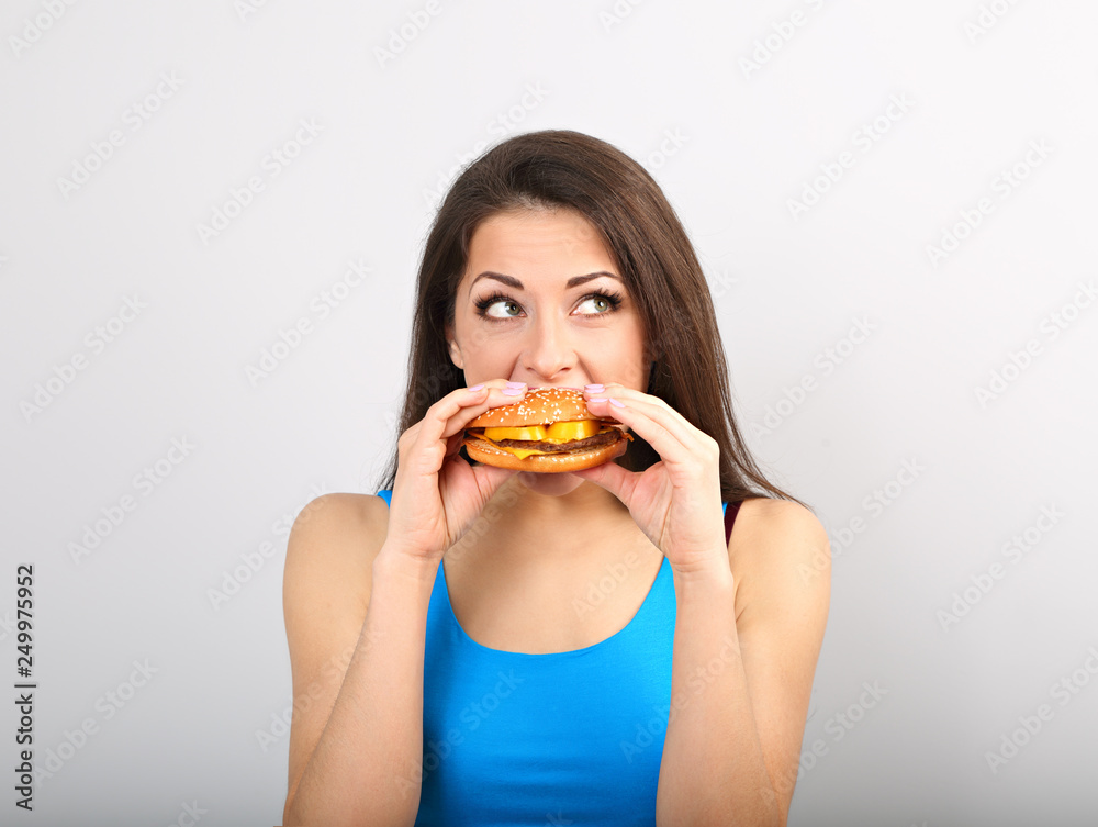 Thinking funny excited woman eating burger on blue background. Closeup portrait Thinking funny excited woman eating burger on blue background. Closeup portrait