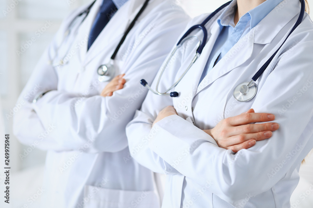 Team of unknown doctors standing straight with arms crossed in hospital. Physicians ready to help. Healthcare, insurance and medicine concept Team of unknown doctors standing straight with arms crossed in hospital. Physicians ready to help. Healthcare, insurance and medicine concept