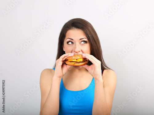 Thinking funny excited woman eating burger on blue background. Closeup portrait