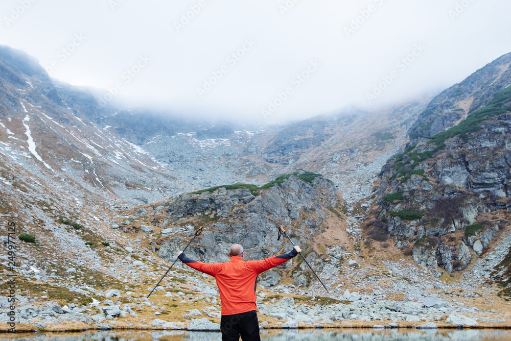 The young man of sporting physique stands on a mountain near the lake