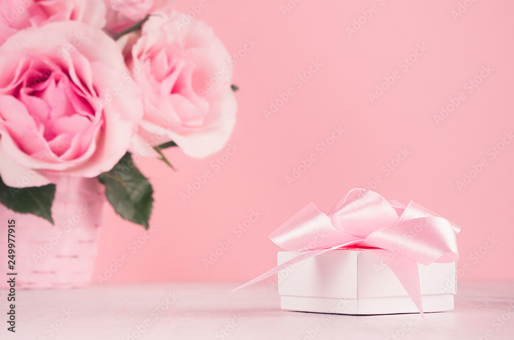 Gentle home decor for Valentines day - roses bouquet and soft light pink gift box with ribbon on white wood board, closeup.