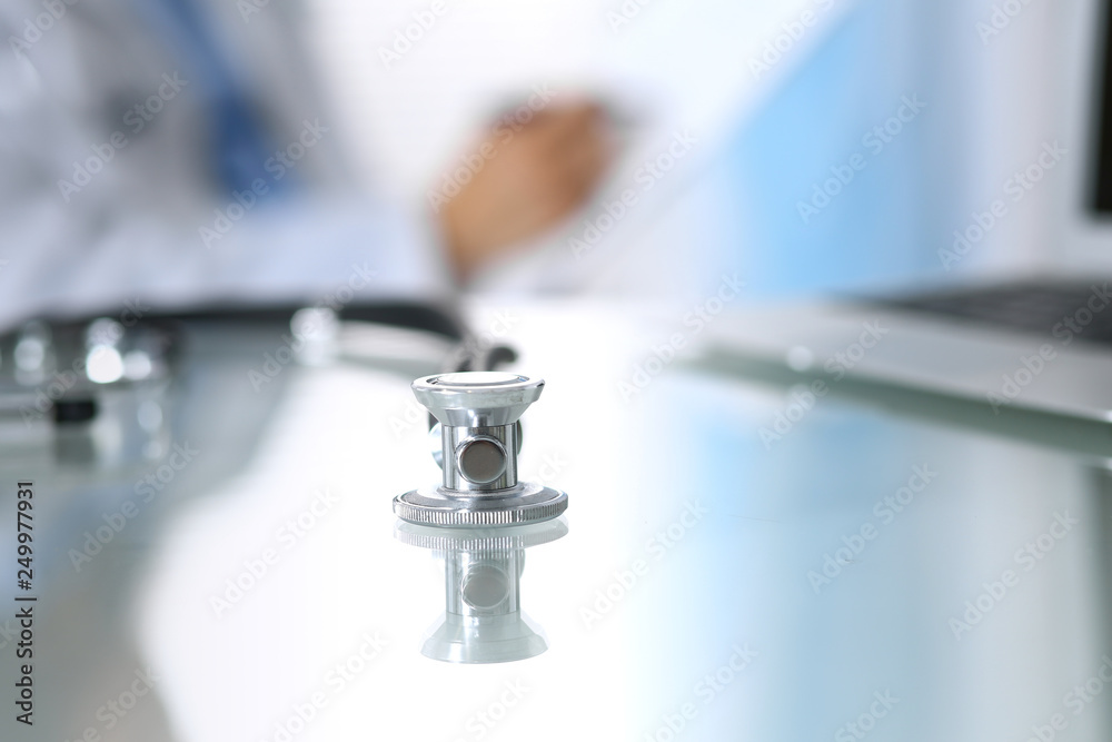 Stethoscope lying on glass desk with laptop computer at busy physician background. Medicine or pharmacy concept. Medical tools at doctor working table Stethoscope lying on glass desk with laptop computer at busy physician background. Medicine or pharmacy concept. Medical tools at doctor working table