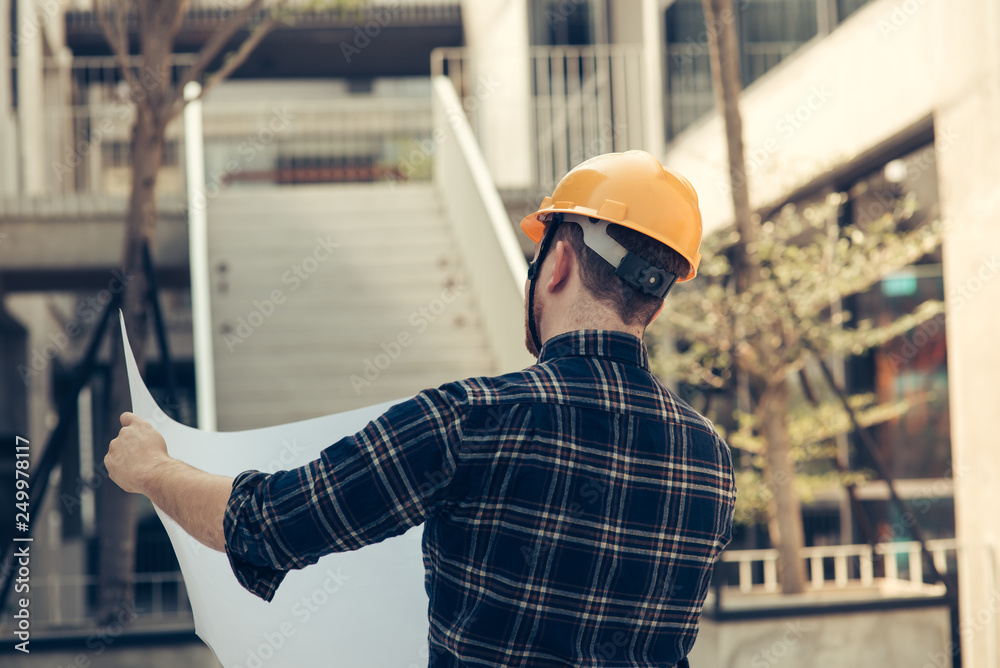 Back of engineer holding blueprint with building background. Back of engineer holding blueprint with building background.