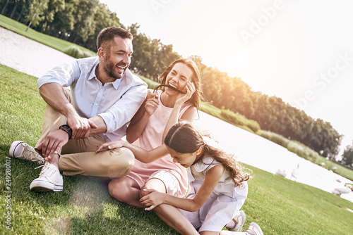 Bonding, Family of three sitting on grassy field having fun laug