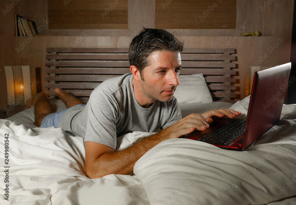 young attractive and relaxed man networking at home lying comfortable on bed late night happy watching movie on laptop computer or enjoying internet social media young attractive and relaxed man networking at home lying comfortable on bed late night happy watching movie on laptop computer or enjoying internet social media
