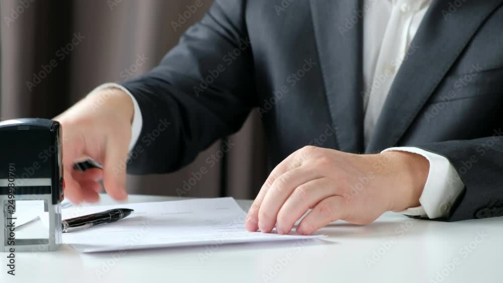 Close-up Of Businessman Hand Signing and Pressing a Stamp On Document in the office Close-up Of Businessman Hand Signing and Pressing a Stamp On Document in the office