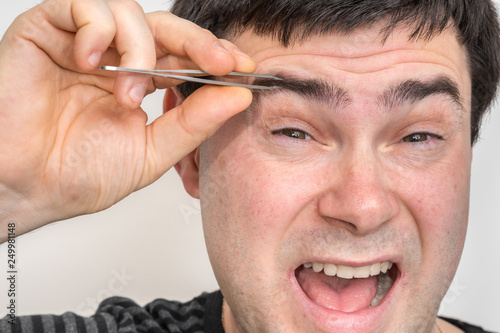 Man is plucking eyebrows with tweezers