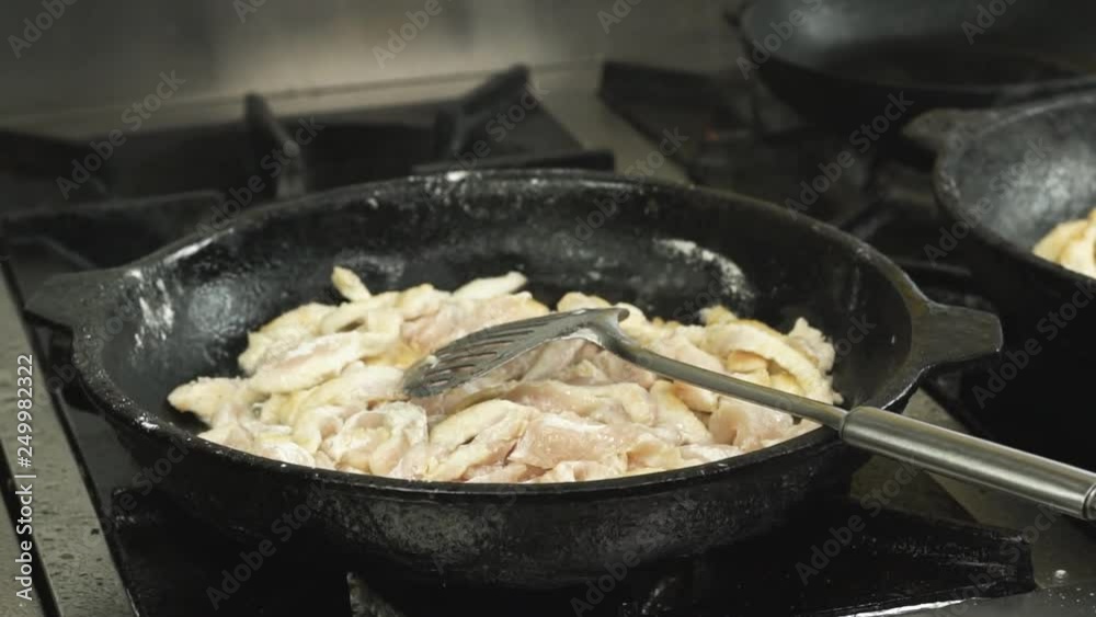 pieces of chicken fillet meat are fried or cooked in a frying pan or skillet in restaurant kitchen on gas stove in slow motion pieces of chicken fillet meat are fried or cooked in a frying pan or skillet in restaurant kitchen on gas stove in slow motion
