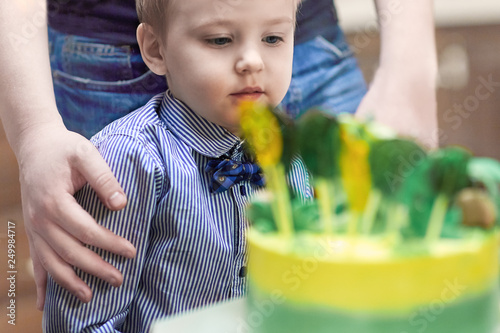 Cute caucasian blonde boy with Birthday cake, his father on bluured background. Happy Birthday and parenthood concept. Indoors, selective focus, copy space. photo