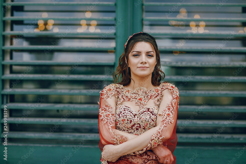 A beautiful Turkish girl in a long red dress walks in the summer old city