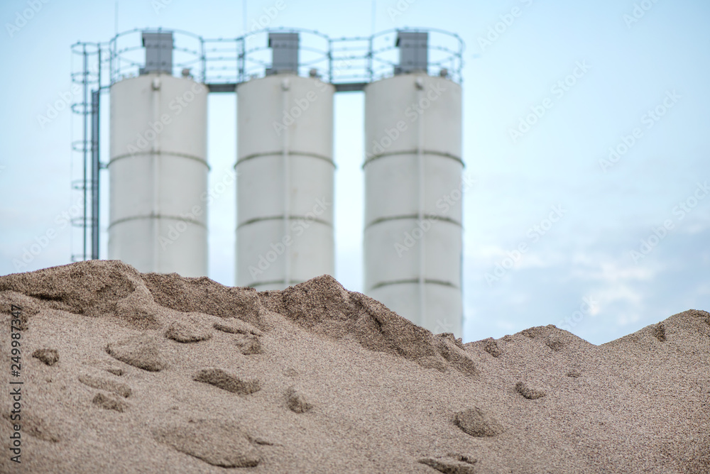 Obraz premium Large piles of construction sand and gravel used for asphalt production and building. Limestone quarry, mining rocks and stones. Factory in the background. Empty space for text of logo 