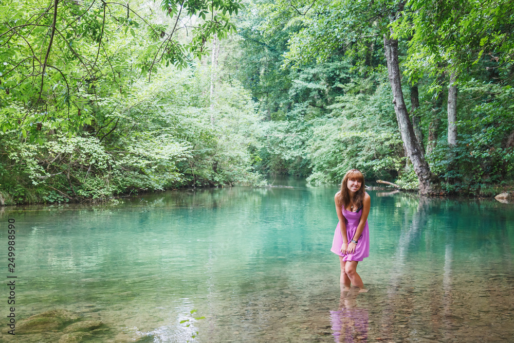Fototapeta premium girl in a pink short dress walks on a river in the forest