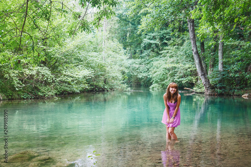 girl in a pink short dress walks on a river in the forest