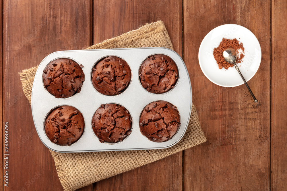 Chocolate muffins in a mould, shot from the top on a dark rustic wooden background with cocoa powder and copy space