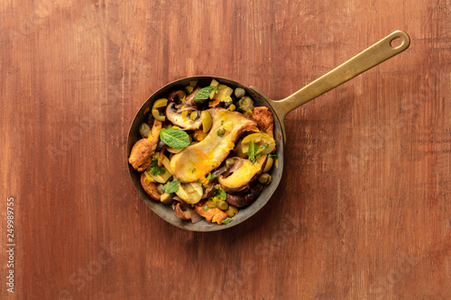 A photo of a rustic mushrooms and olives saute with mint, shot from above on a dark rustic background with copy space