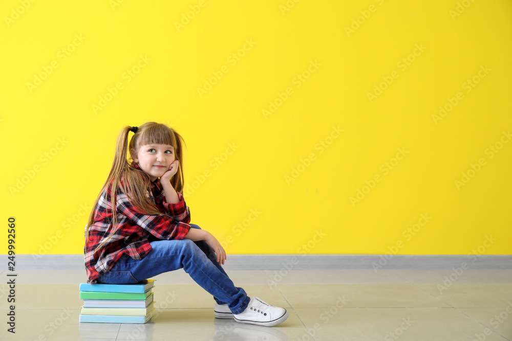 Cute little girl sitting on stack of books against color wall Cute little girl sitting on stack of books against color wall