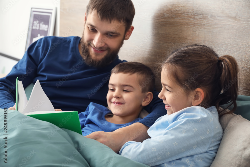 Young father reading book for his children in bed Young father reading book for his children in bed