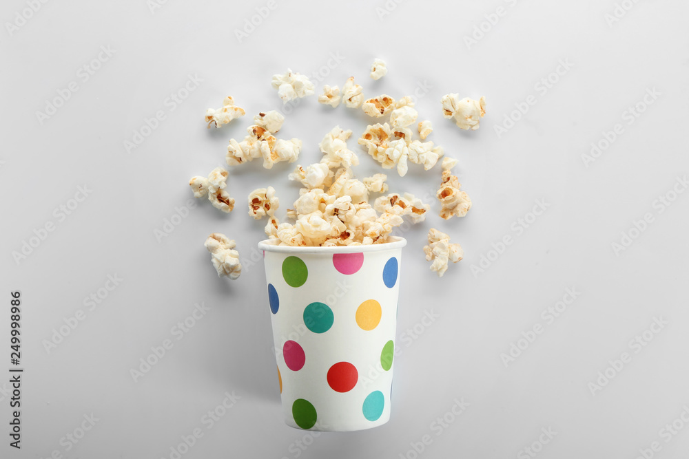 Overturned paper cup of tasty popcorn on white background