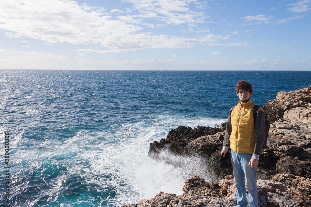 man tourist in yellow vest with backpack on rock cliff in Malta