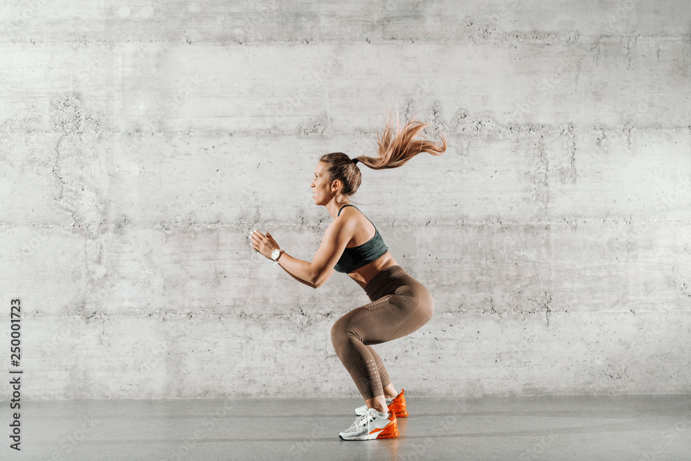 Side view of muscular focused brunette with ponytail and in sportswear  jumping in front of brick wall in gym. Stock 写真 | Adobe Stock
