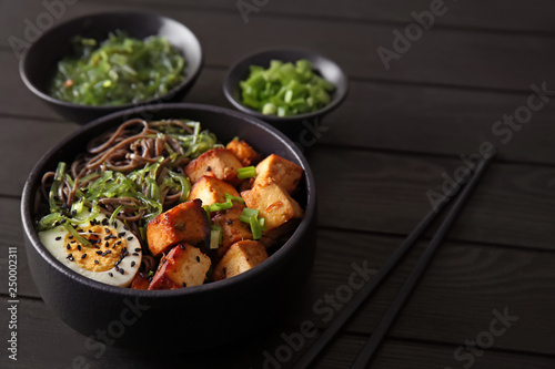 Bowl with tasty fried tofu cheese and soba noodles on table