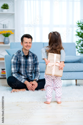 Cute little girl, daughter, sister gives a gift box to young dad father or brother. Both are smiling. Father's day holiday concept, Children's Day