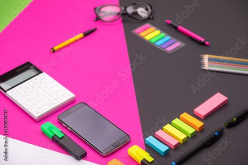 Picture of modern workplace with calculator, markers, stationery and smartphone with copyspace on pink and black background