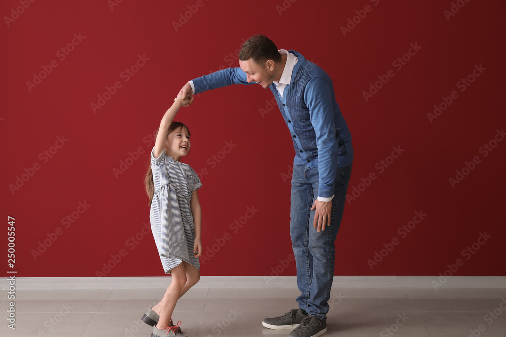 Father and his cute little daughter dancing near color wall