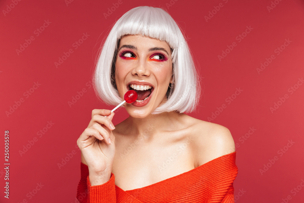 Beautiful young woman isolated over red wall background holding lollipop candy. Beautiful young woman isolated over red wall background holding lollipop candy.