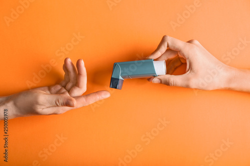 Female hands with inhaler against asthma on color background photo