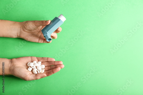 Female hands with inhaler and pills against asthma on color background