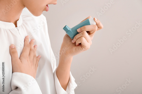 Young woman using inhaler against asthma on light background photo