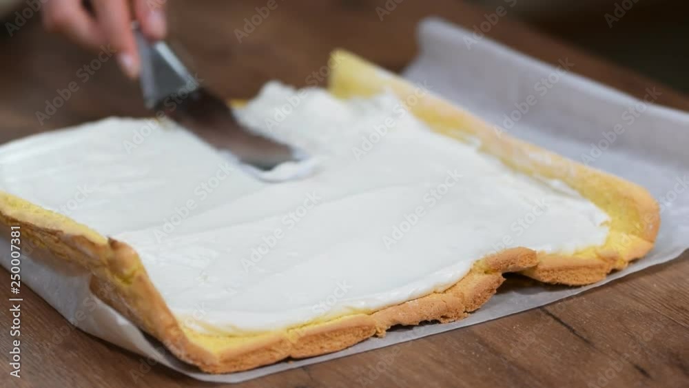 Close up, hands of unrecognizable confectioner spreading cream on sponge cake when making swiss roll at home. Close up, hands of unrecognizable confectioner spreading cream on sponge cake when making swiss roll at home.