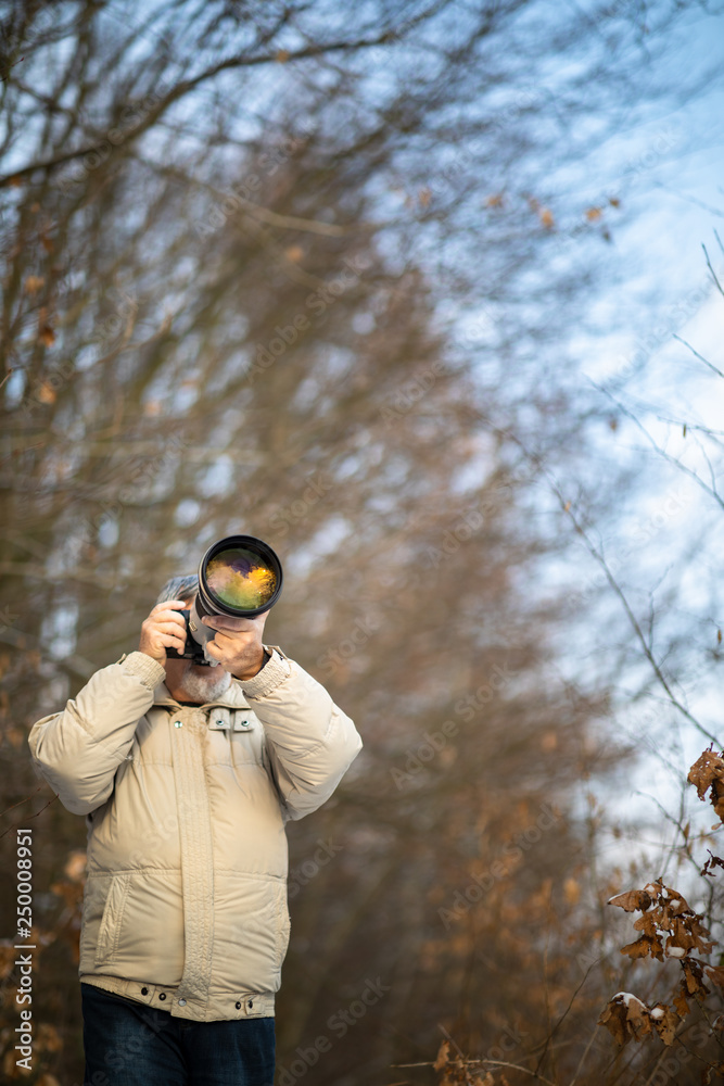 Senior man devoting time to his favorite hobby - photography - taking photos outdoor with his digital camera/DSLR and a big telephoto lens Senior man devoting time to his favorite hobby - photography - taking photos outdoor with his digital camera/DSLR and a big telephoto lens