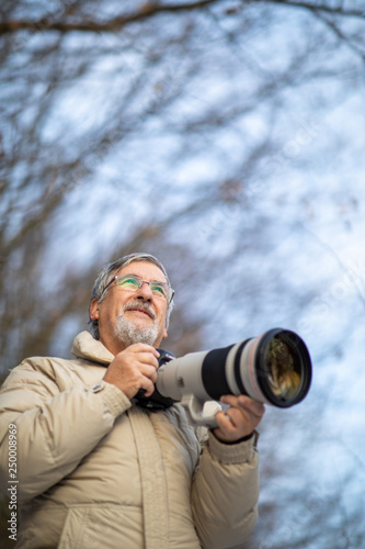 Senior man devoting time to his favorite hobby - photography - taking photos outdoor with his digital camera/DSLR and a big telephoto lens