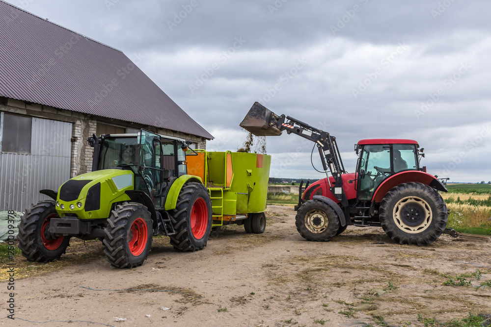 Tractor with front end loader loads the food into a distributor of animal feed for cows. Necessary equipment for a dairy farm. Tractor with front end loader loads the food into a distributor of animal feed for cows. Necessary equipment for a dairy farm.