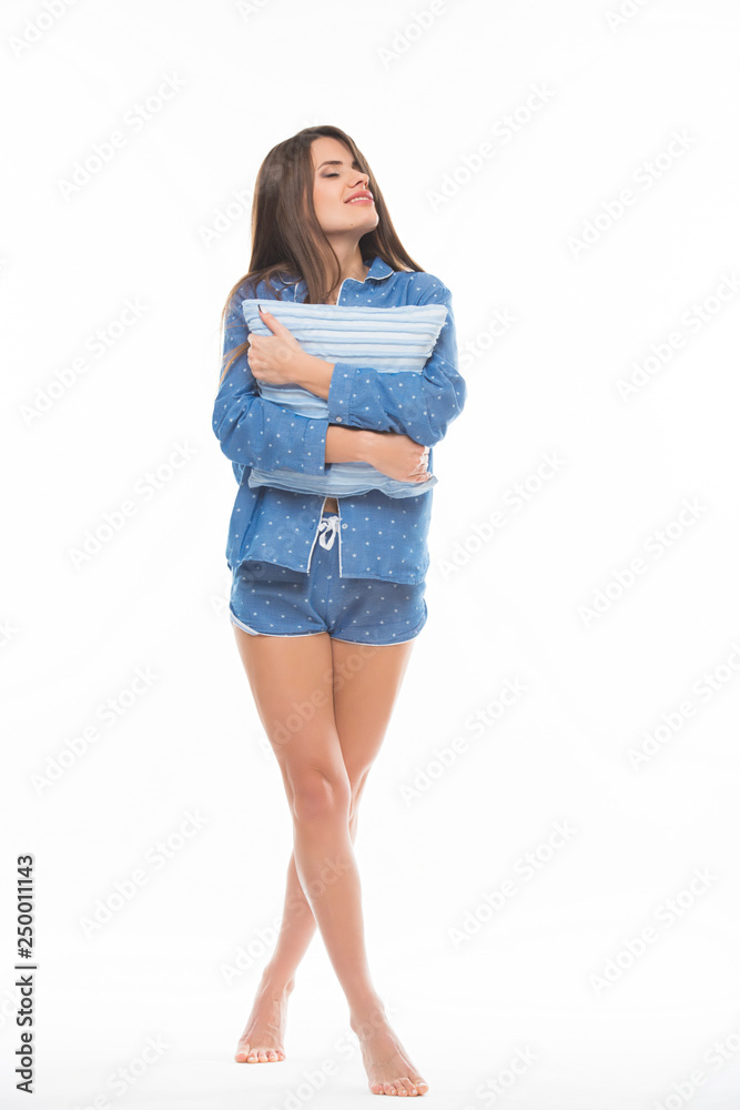 Portrait of a lovely young girl in pajamas hugging a pillow and looking at camera isolated white background Portrait of a lovely young girl in pajamas hugging a pillow and looking at camera isolated white background