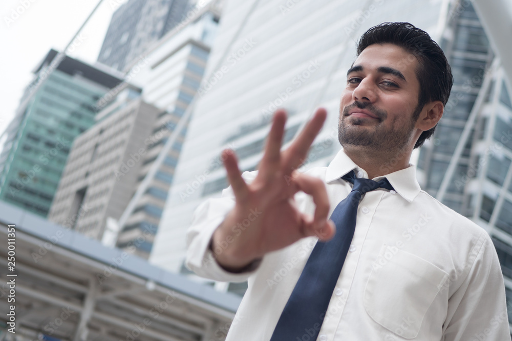 asian business man pointing ok gesture; portrait of Asian, north indian successful and confident businessman points his approving, yes, ok or okay hand sign asian business man pointing ok gesture; portrait of Asian, north indian successful and confident businessman points his approving, yes, ok or okay hand sign