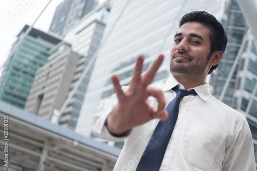 asian business man pointing ok gesture; portrait of Asian, north indian successful and confident businessman points his approving, yes, ok or okay hand sign