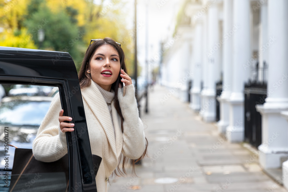 Fototapeta premium Attraktive Geschäftsfrau mit Handy in der Hand steigt aus einem schwarzen Taxi in London 