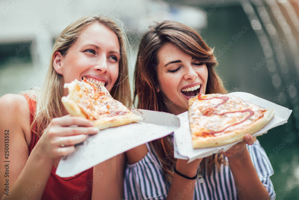 Two beautiful young women eating pizza after shopping, having fun together. Two beautiful young women eating pizza after shopping, having fun together.