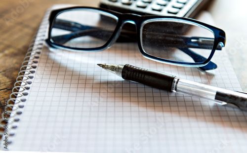 Pen, eyeglasses and calculator on notebook. Close up, study, business and education concept. Image slightly blurred on foreground and background