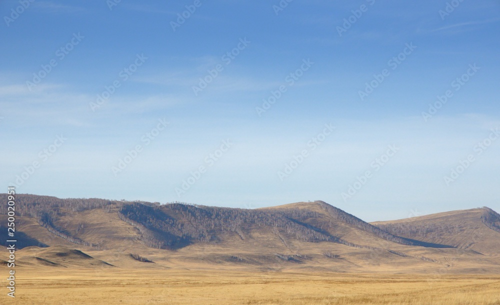 Smooth hills covered with dry grass on horizon with blue sky in Khakassia, Russia