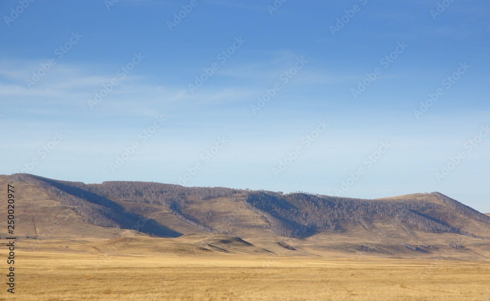 Smooth hills covered with dry grass on horizon with blue sky in Khakassia, Russia