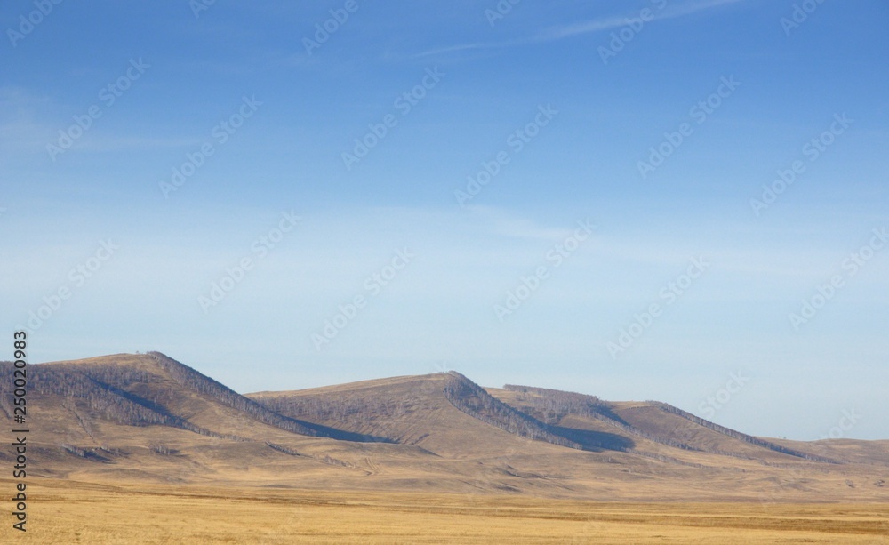 Smooth hills covered with dry grass on horizon with blue sky in Khakassia, Russia Smooth hills covered with dry grass on horizon with blue sky in Khakassia, Russia
